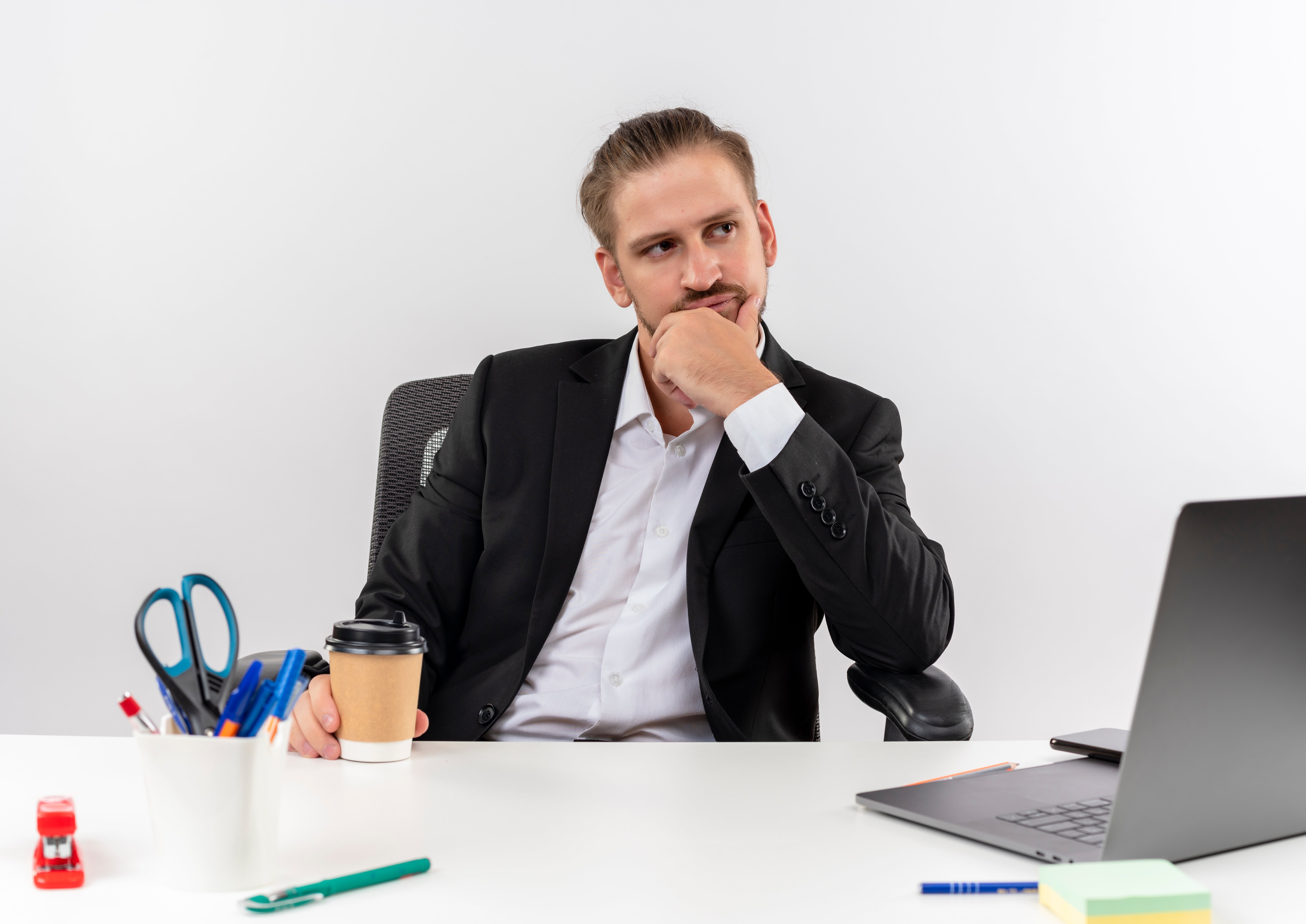 apuesto-hombre-negocios-traje-taza-cafe-mirando-lado-perplejo-sentado-mesa-offise-sobre-fondo-blanco